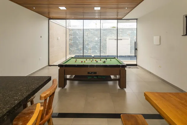 Mesa de sinuca no salão envidraçado, com a piscina atrás do vidro