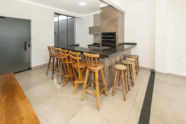 Balcão com banquetas e a churrasqueira de pedra ao fundo