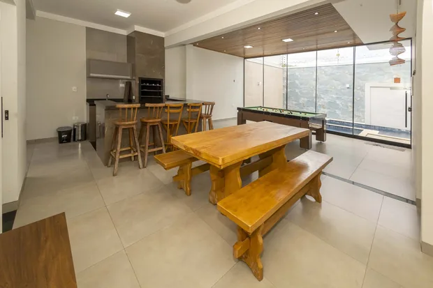 Salão com mesa de madeira, banquetas no balcão e a churrasqueira