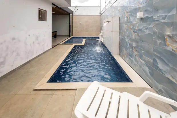Piscina comprida junto à parede de pedra, com a cascata e uma espreguiçadeira