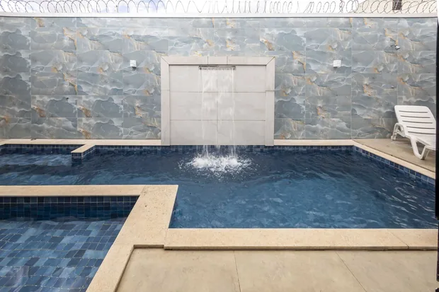 Piscina com a cascata caindo junto à parede de pedra