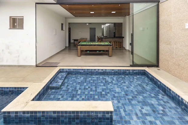 Piscina com o salão envidraçado e a mesa de sinuca ao fundo