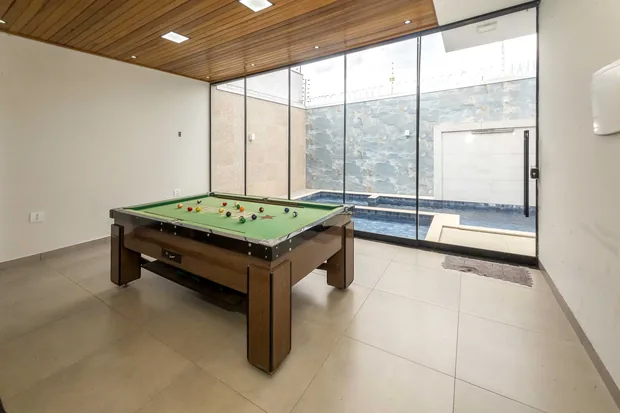 Mesa de sinuca no salão com a porta de vidro aberta para a piscina