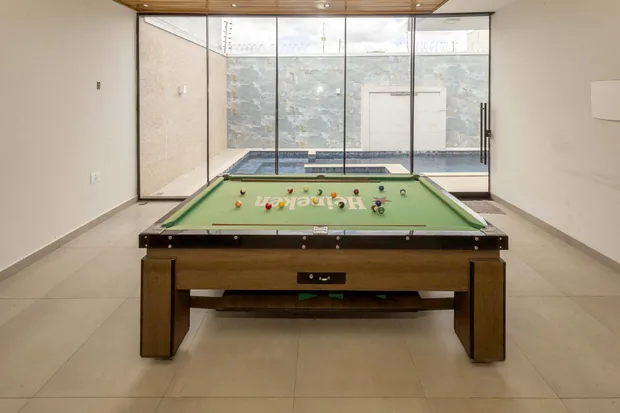 Mesa de sinuca no salão envidraçado, com a piscina atrás do vidro