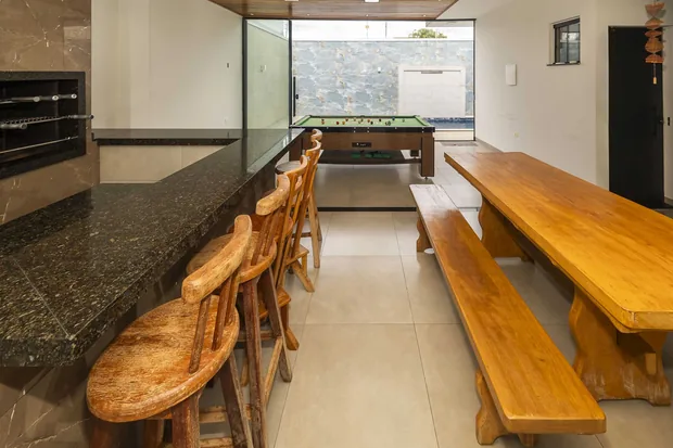 Bancada de granito com banquetas e a mesa comprida de madeira com bancos