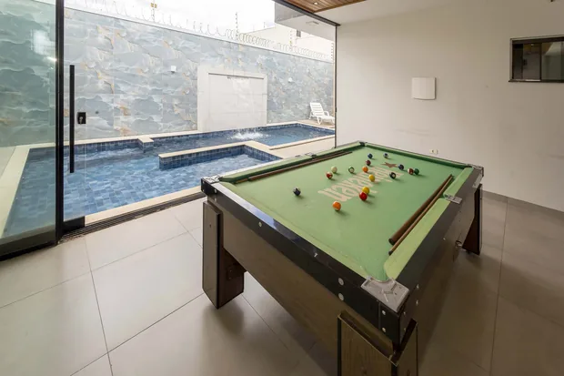 Piscina vista de dentro do salão, com a mesa de sinuca junto ao vidro