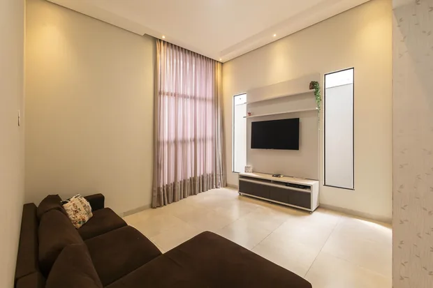 Sala com sofá, painel de TV e cortinas